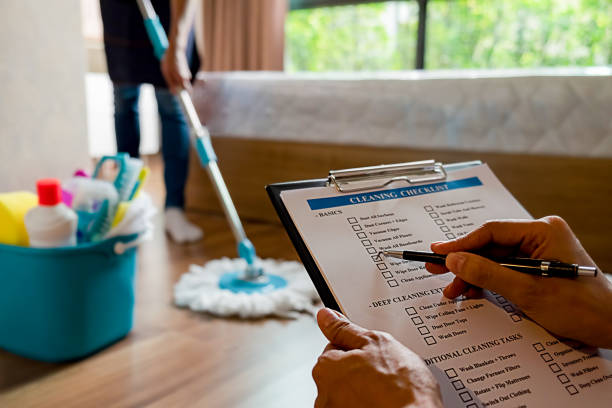 Professional cleaner mopping floors at home as supervisor reviews on clipboard, ensuring quality service.