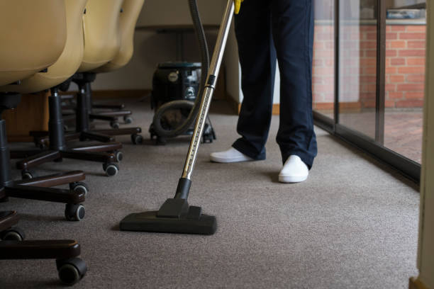 Man cleaning a rug with a vacuum cleaner, in an office, with his uniform, smiling, happy with his work