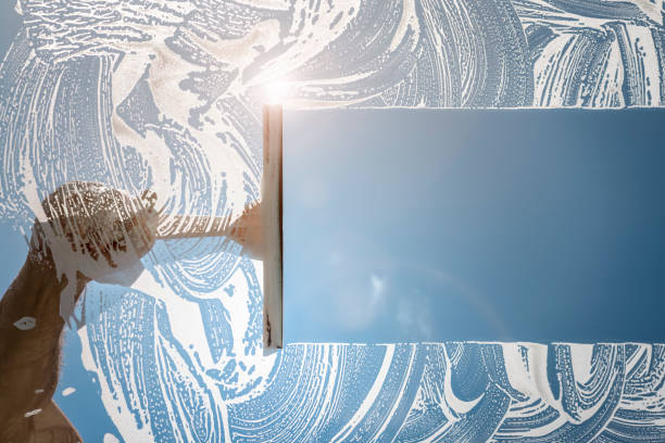 A Male cleaner using a squeegee to wash a window with clear blue sky.