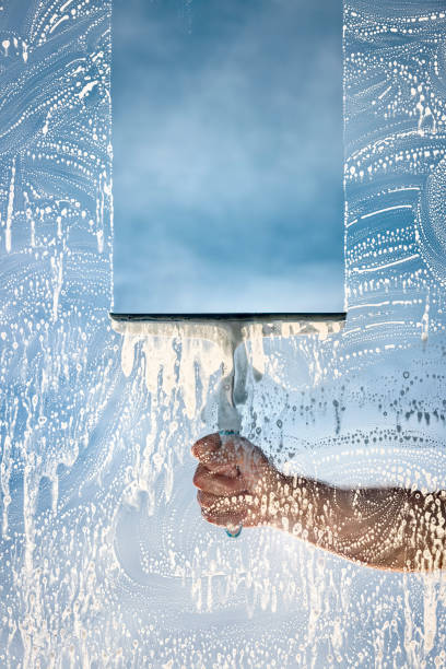 A technician using a squeegee to clean a window under a bright, clear blue sky.