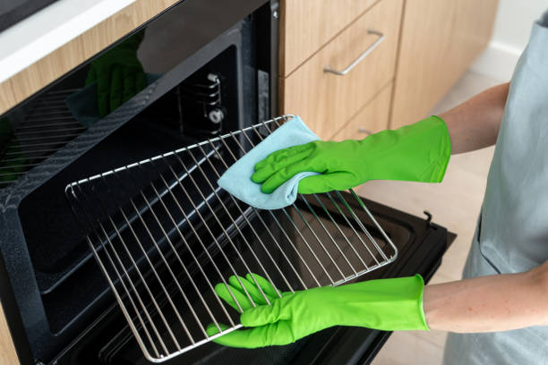 High angle of woman in gloves cleaning oven grill with cloth