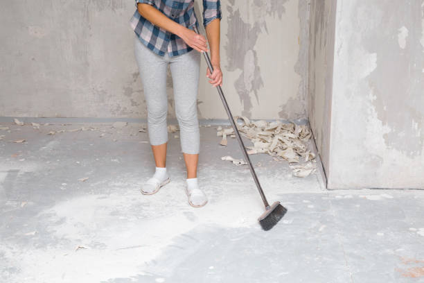 Young woman sweeping white concrete dust from the floor after home repairs, showcasing efficient floor cleaning services.