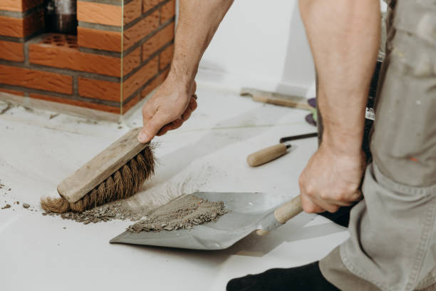 A close-up side view shows a builder collecting cement debris into a dustpan while working on brickwork.