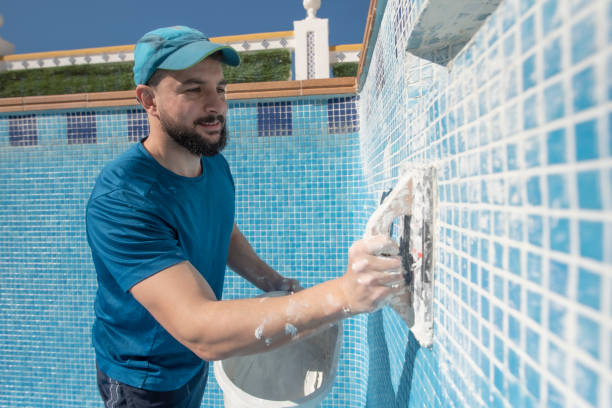 Man spreads the cement grout on the pool tile to waterproof it