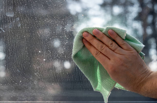 Cleaner cleaning a window glass with water & towel.