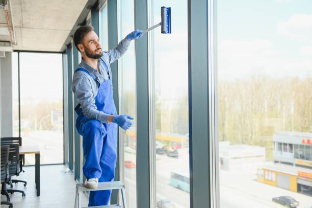 A young man cleaning a window in office.