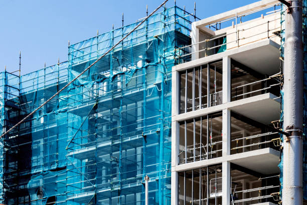 The building's exterior is covered with blue scaffolding fabric for dust control and safety during the construction site cleanup.