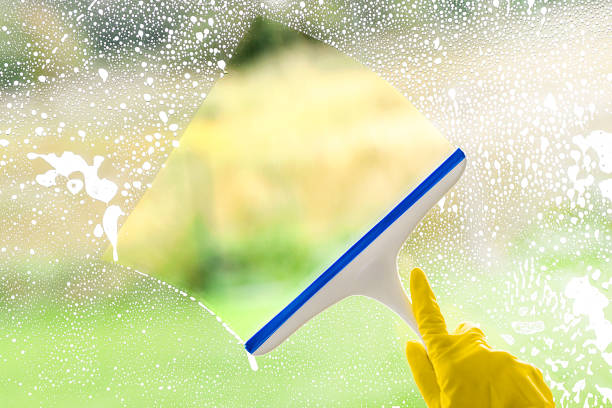 A cleaner focused on washing a window with a squeegee, with water drops visible on the glass