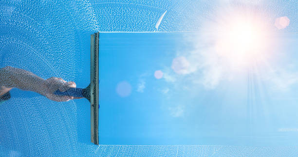 A professional cleaner cleaning a window with squeegee and wiper on a sunny day.