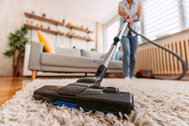 Beautiful young lady vacuuming the home carpet in her apartment.