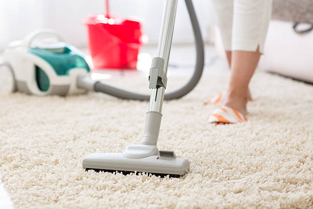 A female cleaner is cleaning a house carpet with a wireless vacuum cleaner.