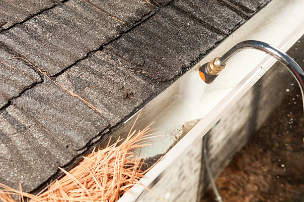 A house rain gutter is being cleaned with a specialized curved pressure washer.