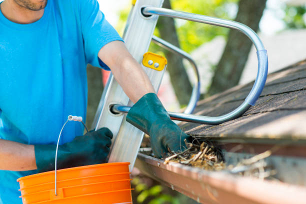 Closeup view of an worker standing on a ladder cleaning gutters.