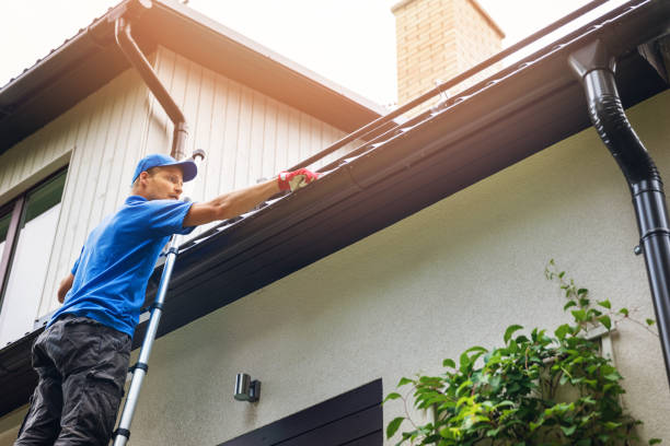 Man on ladder cleaning house gutter from leaves and dirt.