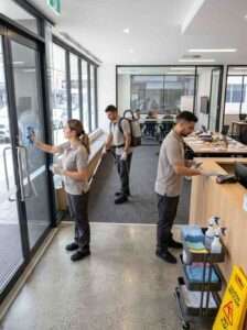 Three professional cleaners From Westlink Cleaning Services working inside a high-traffic office near Bondi Junction, cleaning reception glass, vacuuming walkways, and sanitising reception surfaces.