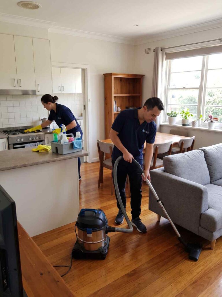 Two cleaners completing house cleaning in an established Burwood home, with one vacuuming timber floors and another cleaning the kitchen stovetop.