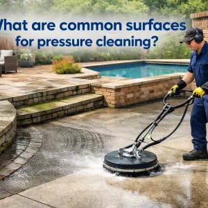 A professional pressure cleaning technician washing a concrete driveway and surrounding outdoor surfaces, including pavers and patio areas.