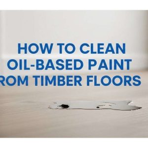 Professional blog thumbnail showing a timber floor with a small paint spill and a bold title about cleaning oil-based paint.