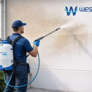 Professional cleaner soft washing a rendered and painted exterior wall in a realistic residential setting
