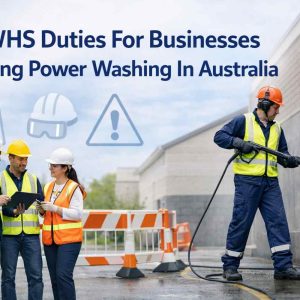 Professional worker safely power washing a surface with PPE and safety barriers, WHS duties for businesses in Australia.